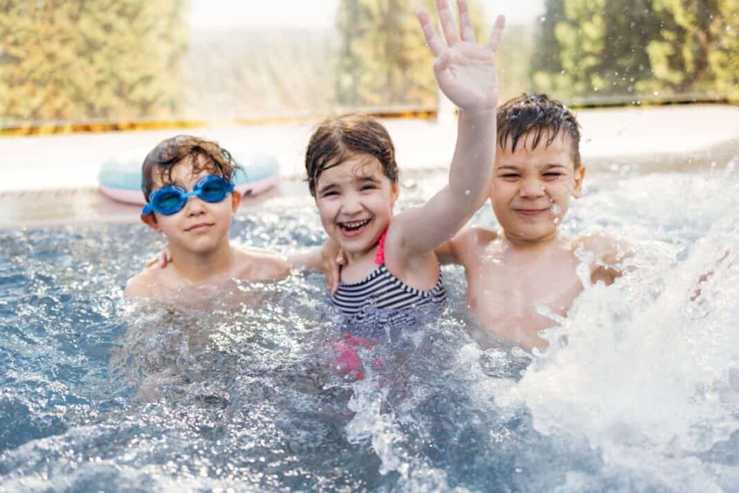 Three small children are swimming in the outdoor Jacuzzi pool. Cute kids cuddle and have fun in the swirling water. Wie souverän sind Kinder im Wasser?