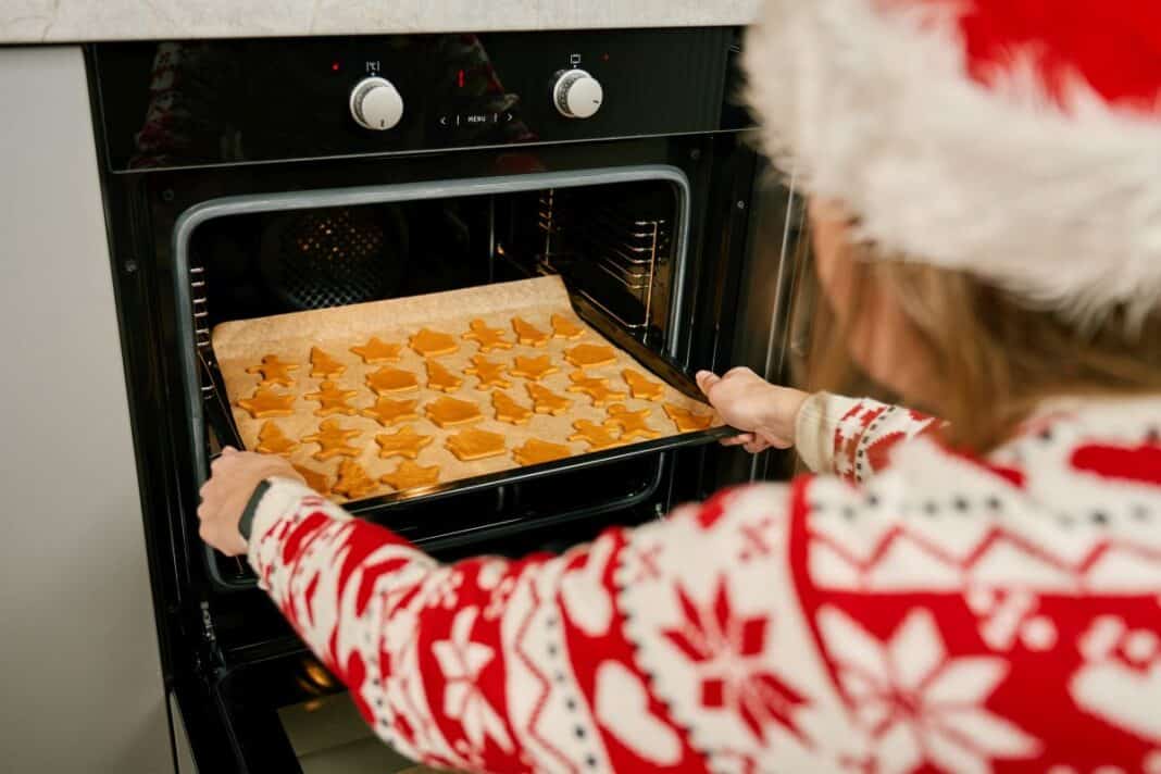 Woman in festive sweater baking Christmas cookies in oven Besinnlichkeit statt Brandalarm: Tipps für eine sichere Adventsküche